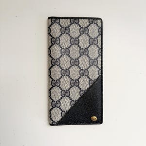 May include: A black and white patterned leather wallet with a black leather flap and a gold-toned logo.