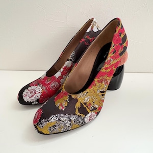 May include: A pair of black high-heeled shoes with a floral pattern in red, yellow, and white. The heels are chunky and have a unique design.