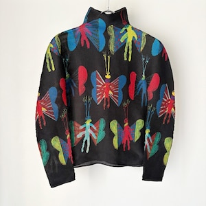 Puede incluir: Top negro de manga larga con cuello alto. El top está estampado con diseños de mariposas coloridas en rojo, azul, amarillo y verde. Las mariposas tienen un estilo caprichoso y artístico.