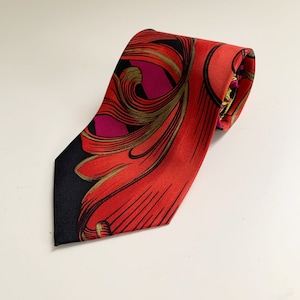 Puede incluir: Una corbata de seda con un diseño floral rojo, negro y dorado.