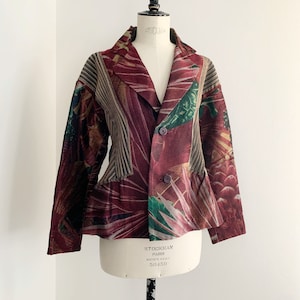Könnte beinhalten: Ein rot, grün und braun gemusterter Blazer mit doppelreihigem Verschluss. Der Blazer hat eine figurbetonte Silhouette und einen leicht ausgestellten Saum. Das Etikett auf dem Blazer lautet "Stockman Paris Boutique Verkauft bei 50+150".