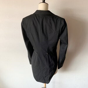 May include: A black tailcoat with a long, pointed back. The coat has a single button closure at the waist and two buttons on the back.