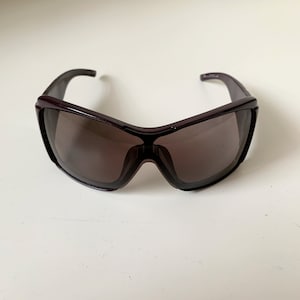 May include: A pair of dark purple sunglasses with a large, wraparound frame and dark lenses.