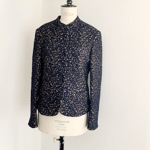May include: A black and cream patterned blazer with a stand-up collar and button closure. The blazer is made of a soft, textured fabric.