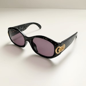 May include: Black sunglasses with a marbled pattern and gold accents. The sunglasses have a rounded shape and a double-C logo on the side.