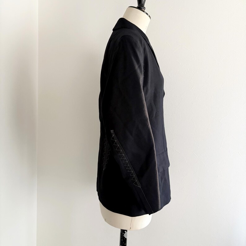 Puede incluir: Blazer negro con solapa de muesca y corte entallado. La chaqueta presenta costuras decorativas a lo largo de la costura lateral. El blazer se exhibe en un maniqu&iacute; sobre un fondo blanco.