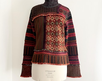 May include: A patchwork sweater with a high neck and long sleeves. The sweater features a variety of patterns, including diamonds, stripes, and geometric shapes, in shades of brown, red, and green. The sweater is displayed on a mannequin.
