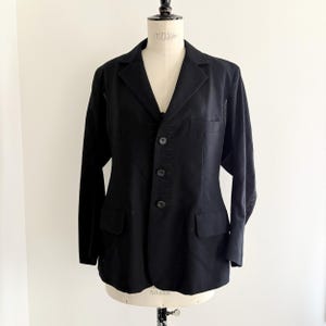 Puede incluir: Un blazer negro con un dise&ntilde;o cl&aacute;sico, con solapa de muesca, cierre de tres botones y dos bolsillos delanteros. Las mangas largas tienen costuras decorativas cerca de los pu&ntilde;os. El blazer se muestra en un maniqu&iacute;.