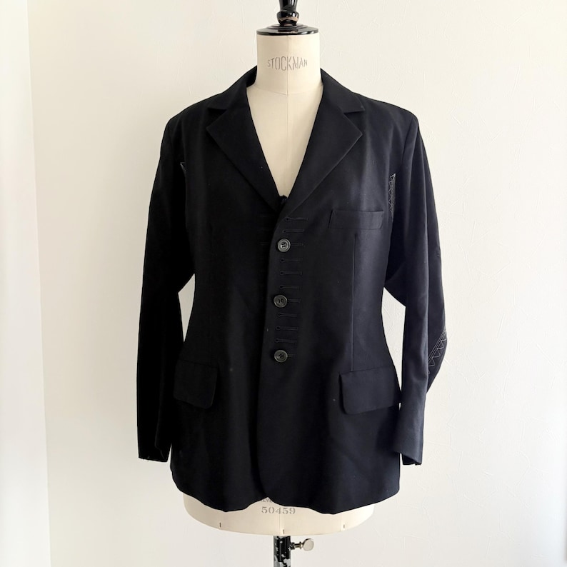 Puede incluir: Un blazer negro con un dise&ntilde;o cl&aacute;sico, con solapa de muesca, cierre de tres botones y dos bolsillos delanteros. Las mangas largas tienen costuras decorativas cerca de los pu&ntilde;os. El blazer se muestra en un maniqu&iacute;.