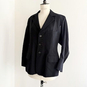 Puede incluir: Un blazer negro con solapa de muesca, tres botones y dos bolsillos delanteros. El blazer tiene costuras decorativas en la parte delantera y en las mangas. La prenda se exhibe en un maniqu&iacute;.