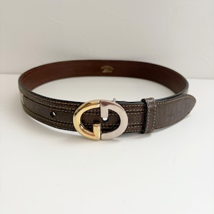 May include: A brown leather belt with a gold and silver double G buckle.