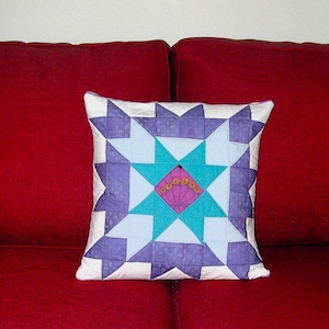 May include: A white pillow with a purple, blue, and teal starburst pattern. The pillow is on a red couch.