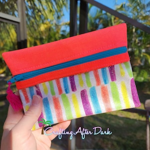 May include: A small, bright pink zippered pouch with a white background and colorful stripes. The stripes are a variety of colors, including purple, blue, green, yellow, and orange. The pouch has a turquoise zipper and a pink tassel.