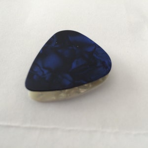 Puede incluir: Una púa de guitarra azul y blanca con un patrón de mármol.
