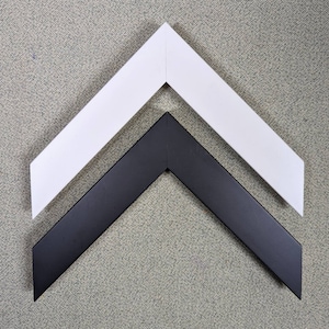 Puede incluir: Dos marcos de fotos, uno negro y otro blanco, están dispuestos en forma de chevron. Los marcos son de madera y tienen un diseño simple y moderno.