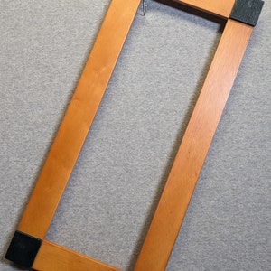 May include: A wooden frame with black corner protectors. The frame is rectangular and has a light brown finish.