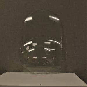 May include: Clear, transparent, curved glass objects of varying sizes are arranged on a white surface. The largest piece is a tall, rounded rectangle. A smaller, circular piece and a curved, semi-circular piece are also visible.