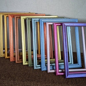 May include: A collection of colorful picture frames in various metallic finishes, including silver, gold, copper, and blue. The frames are arranged in a diagonal line, showcasing their different hues and textures. The frames are empty, ready for photos or artwork.