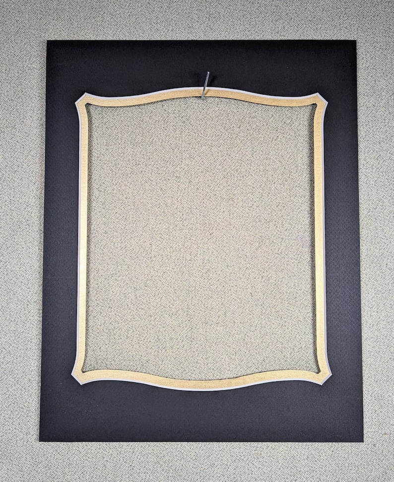 May include: A black mat with a gold and white decorative frame. The frame has a wavy, scalloped design.