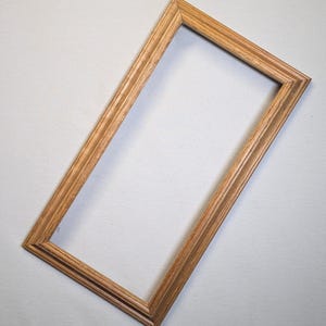 May include: A rectangular wooden picture frame with a light brown finish. The frame has a simple, classic design with a slightly raised inner edge. The frame is empty, ready for a photo or artwork.