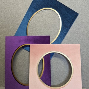 May include: Three rectangular frames with velvet-textured surfaces in blue, purple, and light pink. Each frame features a central circular cutout with a smooth gold-colored inner rim. The frames are layered, with the blue frame at the top, the purple frame in the middle, and the light pink frame at the bottom.