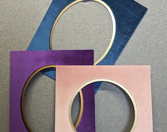 May include: Three rectangular frames with velvet-textured surfaces in blue, purple, and light pink. Each frame features a central circular cutout with a smooth gold-colored inner rim. The frames are layered, with the blue frame at the top, the purple frame in the middle, and the light pink frame at the bottom.