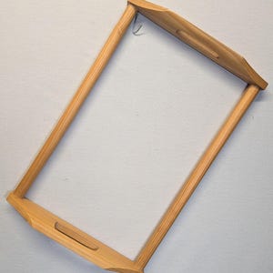 May include: A rectangular, light-colored wooden tray with a handle cut into each of the four sides. A small metal hook is attached to the top edge. The tray is made of light-colored wood.