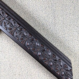 May include: Close-up of a black picture frame with a decorative floral design. The frame is made of wood and has a smooth finish.