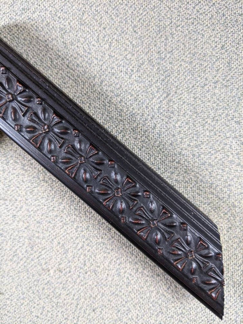 May include: Close-up of a black picture frame with a decorative floral design. The frame is made of wood and has a smooth finish.