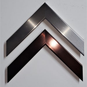 May include: Two metal picture frames, one silver and one copper, are arranged in a chevron pattern. The frames are both angled and have a brushed finish.