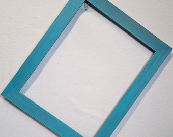 May include: A rectangular picture frame with a distressed teal finish. The frame is empty and ready for a photo or artwork. A small metal hook is attached to the top edge for hanging. The frame is angled against a white background.