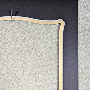 May include: Close-up of a corner of a picture frame with a decorative, scalloped, gold-colored mat. The mat is set against a black background.