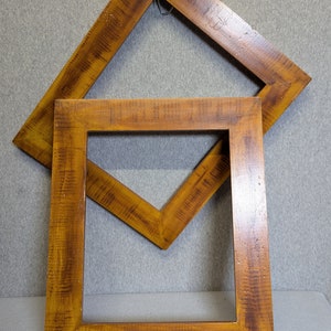 May include: Two wooden picture frames, one on top of the other. The top frame is a diamond shape and the bottom frame is a square. Both frames are a dark brown color.