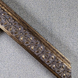 May include: A close-up of a gold picture frame with a decorative floral design. The frame is made of wood and has a distressed finish.