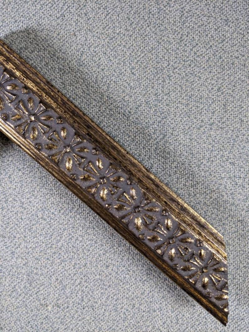 May include: A close-up of a gold picture frame with a decorative floral design. The frame is made of wood and has a distressed finish.