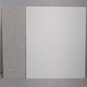 May include: Two rectangular boards covered in fabric. The board on the left is covered in a light beige, textured linen-like material. The larger board on the right is covered in a solid off-white, textured linen-like material with a visible weave.
