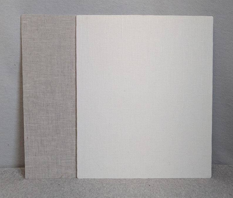 May include: Two rectangular boards covered in fabric. The board on the left is covered in a light beige, textured linen-like material. The larger board on the right is covered in a solid off-white, textured linen-like material with a visible weave.