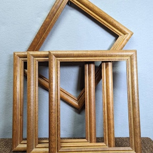May include: Four wooden picture frames in various sizes, stacked on top of each other. The frames are all brown with a light wood grain and have a simple, classic design.