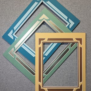 May include: Three picture frames, one inside the other. The outer frame is teal blue with a white inner border. The middle frame is a light green with a silver inner border. The inner frame is a light brown with a dark brown inner border.
