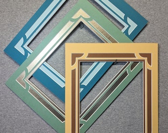 May include: Three picture frames, one inside the other. The outer frame is teal blue with a white inner border. The middle frame is a light green with a silver inner border. The inner frame is a light brown with a dark brown inner border.