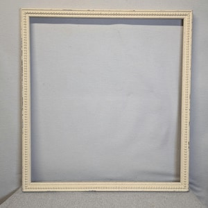 May include: A square, off-white picture frame with a decorative beaded edge. The frame has a distressed finish, with visible wear and tear. The frame is empty, with a neutral background.