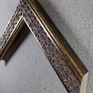 May include: A gold picture frame with a decorative floral design. The frame is made of wood and has a distressed finish.