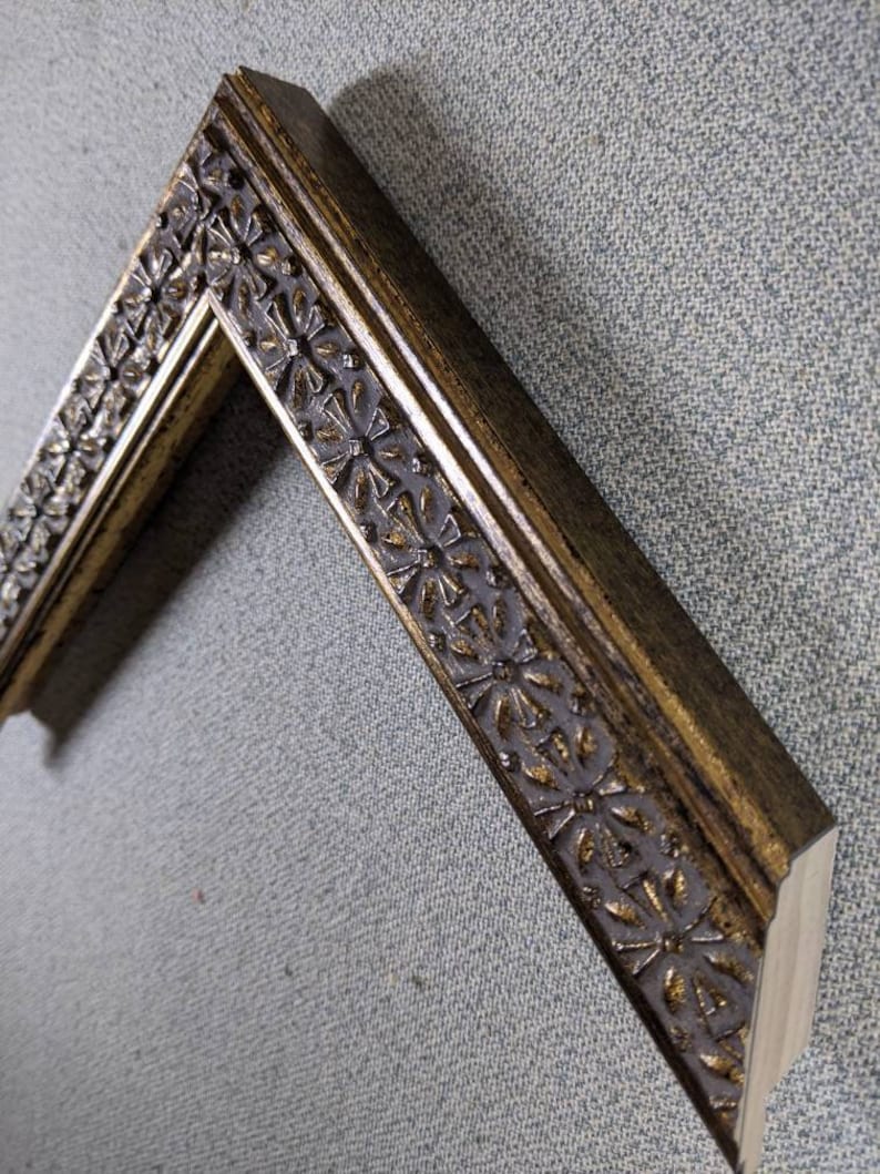 May include: A gold picture frame with a decorative floral design. The frame is made of wood and has a distressed finish.