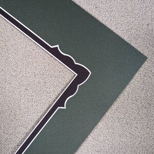 May include: A dark green picture frame mat board featuring a decorative inner edge with a scalloped design. The inner border is accented with a thin white line that outlines the scalloped shape, providing a contrast against the dark green surface.