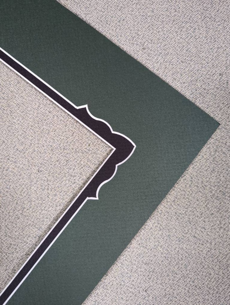 May include: A dark green picture frame mat board featuring a decorative inner edge with a scalloped design. The inner border is accented with a thin white line that outlines the scalloped shape, providing a contrast against the dark green surface.