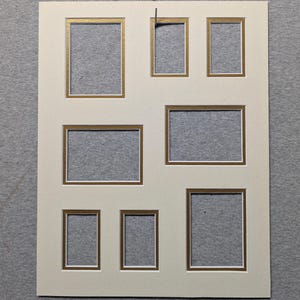 May include: A rectangular off-white photo mat board featuring seven cutouts of varying sizes arranged in a collage layout. Each cutout is bordered by a thin gold metallic trim, providing a decorative frame for displaying multiple photographs.