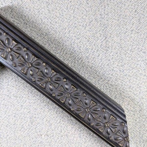 May include: Black picture frame with a decorative, ornate, floral design. The frame has a beveled edge and a dark, almost black, finish.