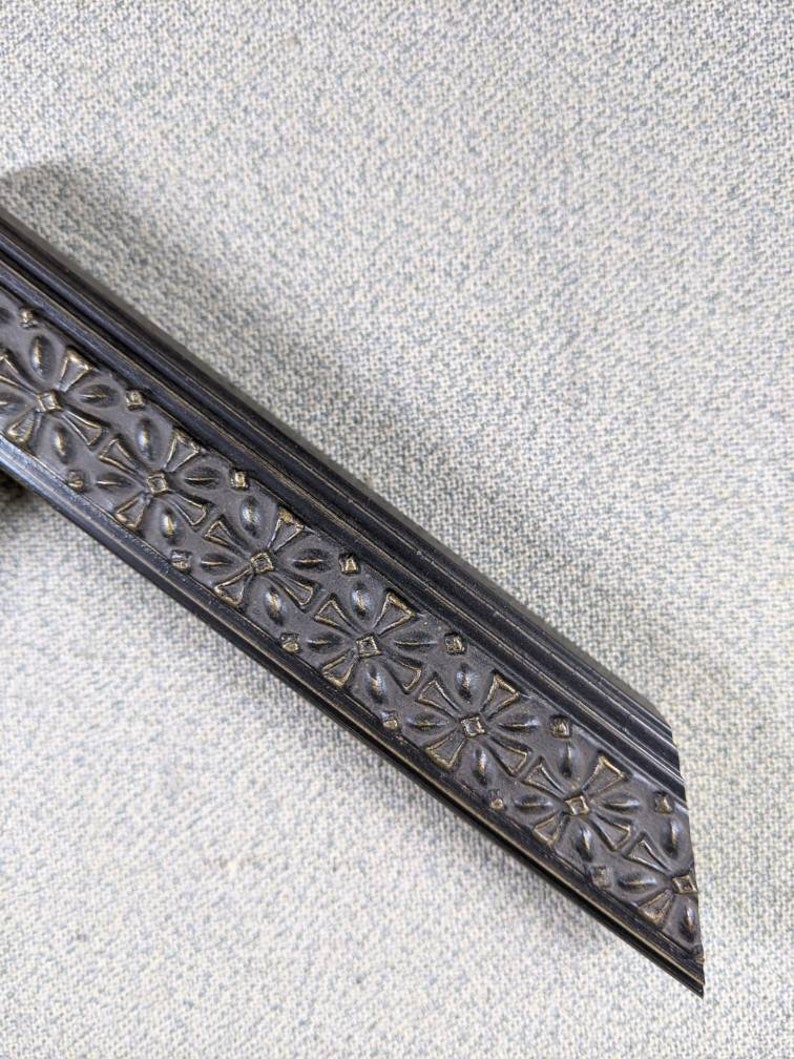 May include: Black picture frame with a decorative, ornate, floral design. The frame has a beveled edge and a dark, almost black, finish.