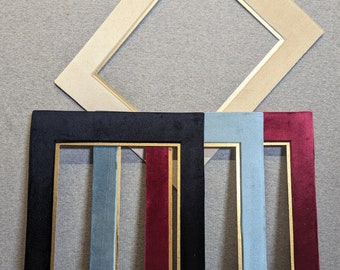 May include: A collection of four rectangular picture frames. One frame is beige, while the other three are covered in velvet fabric in black, light blue, and deep red. Each frame features a thin gold-colored inner border around the opening.