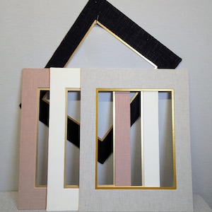 May include: A collection of four rectangular picture frame mats featuring a textured fabric finish. The mats are available in black, dusty rose, white, and light gray, each accented with a thin, metallic gold inner border edge.